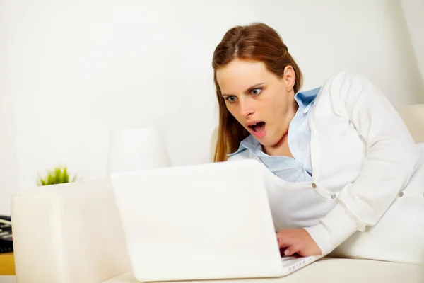 Verrast vrouw liggend op de Bank met een laptop — Stockfoto