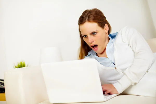 Stock image Surprised woman lying on sofa with a laptop