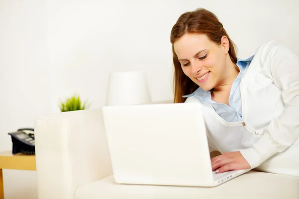 Vrolijke dame liggend op de Bank met een laptop — Stockfoto
