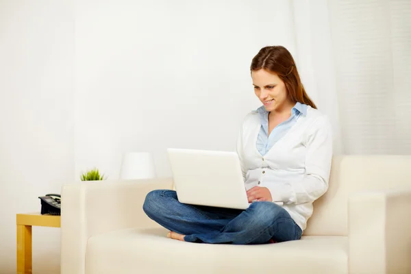 Mujer caucásica trabajando en un sofá con un ordenador portátil —  Fotos de Stock