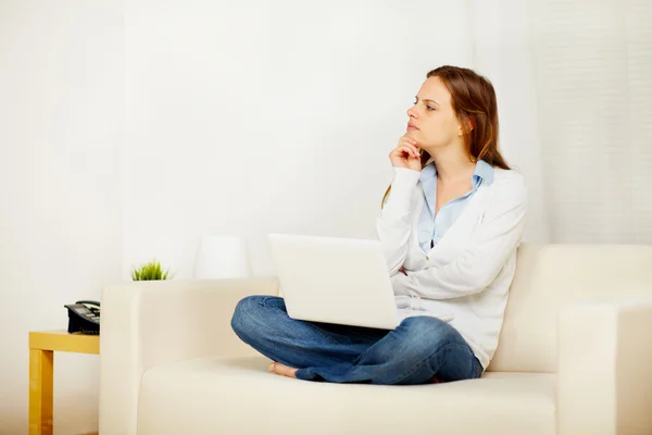 Jovem pensamento feminino no sofá com um laptop — Fotografia de Stock