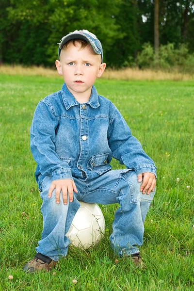 Menino senta-se na bola de futebol — Fotografia de Stock
