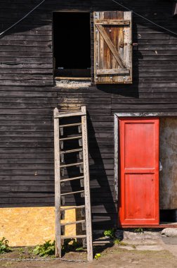 Wooden ladder on a cottage wall with red door clipart