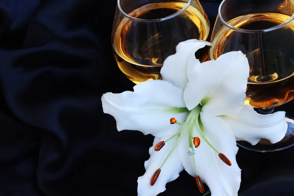 Glasses with wine and lily flower on black silk — Stock Photo, Image