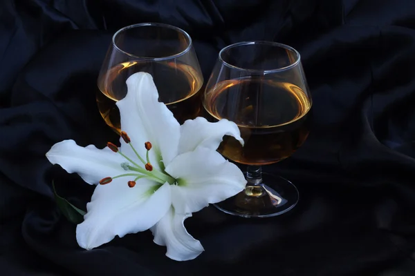 Glazen met wijn en lily bloem op zwarte zijde — Stockfoto