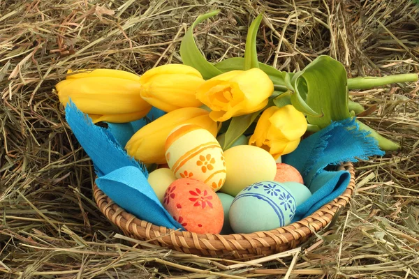 Корзина пасхальных яиц и тюльпанов на сене — стоковое фото