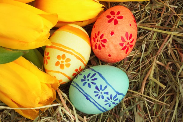 Paskalya yumurtaları ve laleler saman üzerinde — Stok fotoğraf