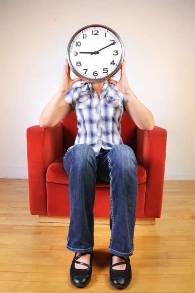 Woman holding a clock covering her face