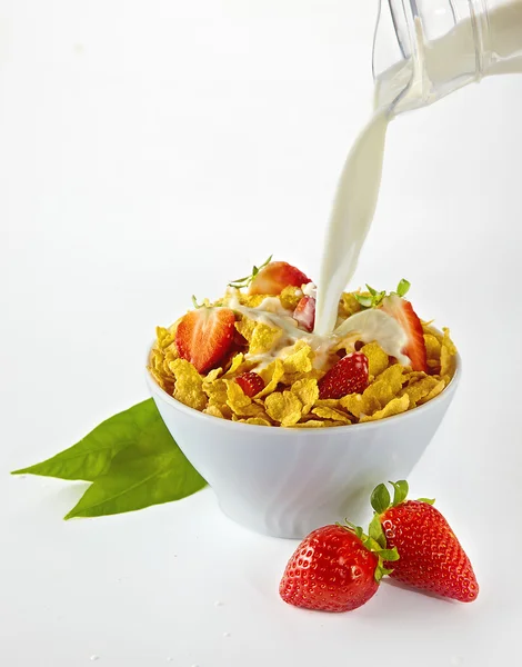 Verter la leche en un tazón rojo de copos de maíz con fresas sobre fondo blanco — Foto de Stock