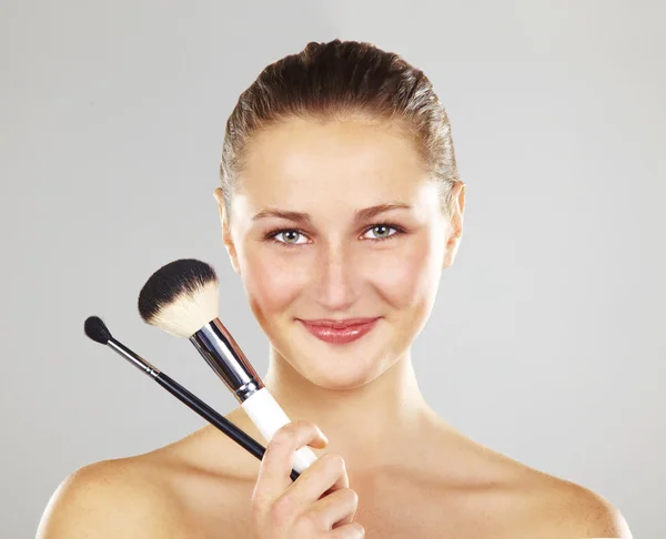Vacker ung kvinna ler innehar make-up borstar. fotomodell poserar över vit bakgrund — Stockfoto