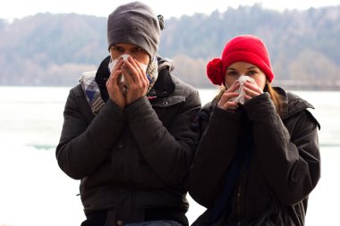 A Young Couple Next To Each Other Blowing Their Noses clipart