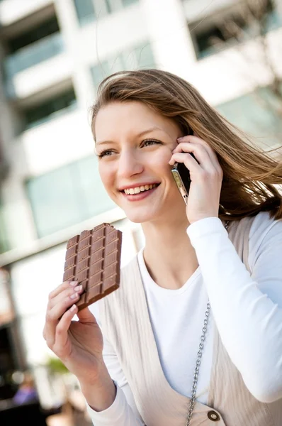 Woman eating chocolate and calling with mobile — Stock Photo, Image