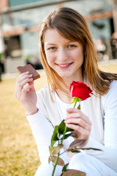 Woman eating chocolate with red rose — Stock Photo, Image