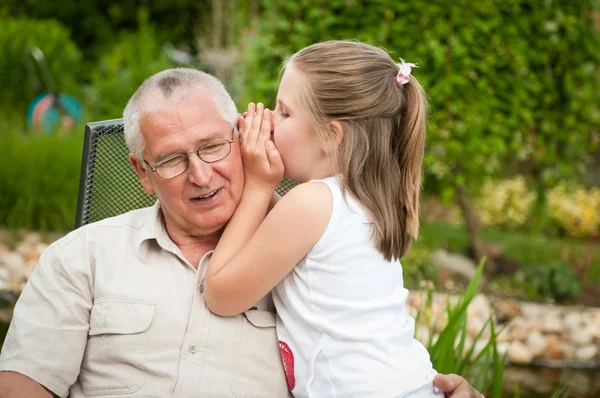 Girl says something in the ear of his grandfather — Stock Photo, Image