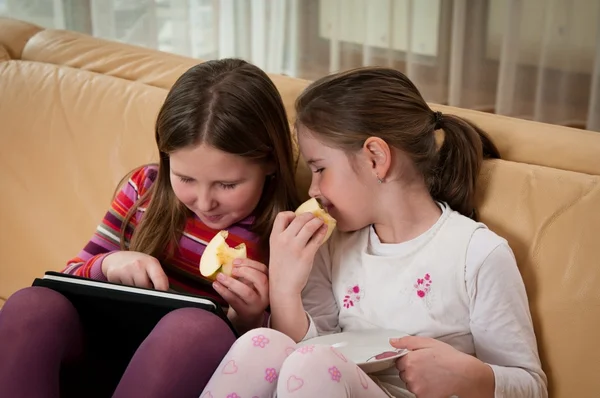 Systrarna leker med tablett och äta äpple — Stockfoto