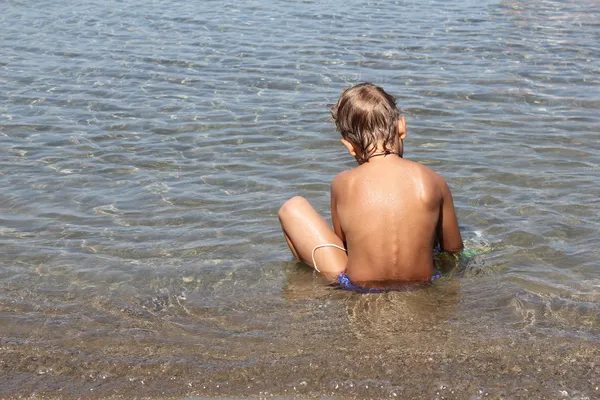 Junge sitzt am tropischen Strand am Wasser Stockbild