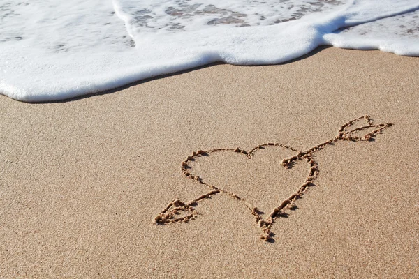 Amor arrow k srdci v písku. — Stock fotografie