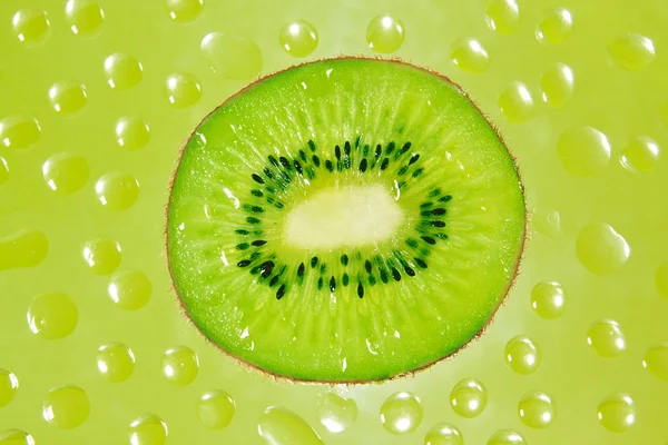 A fresh slice of kiwi fruit in green background drops. — Stock Photo, Image