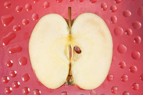 Skiva ett äpple på en röd bakgrund i droppar. — Stockfoto