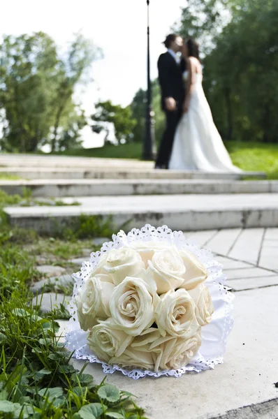 Wedding bouquet with the wedding couple in the background — Stock Photo, Image