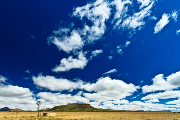 Molino de viento en un paisaje desolado con hermoso paisaje nublado — Foto de Stock