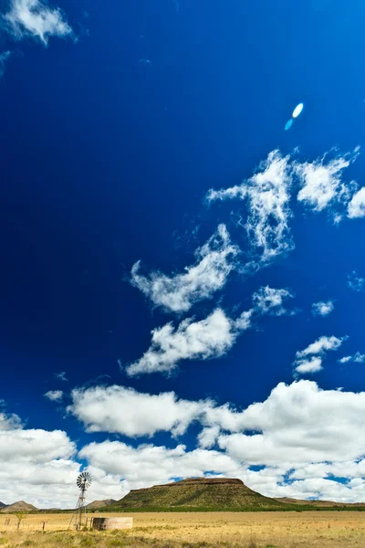 Molino de viento en un paisaje desolado con hermoso paisaje nublado — Foto de Stock