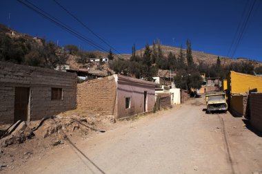 Dusty street with adobe houses and old cars in Tilcara - North Argentina clipart