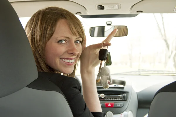 Улыбающаяся молодая девушка в машине показывает ключ — стоковое фото