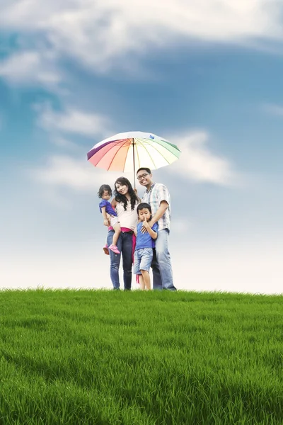 Família feliz com guarda-chuva colorido no prado — Fotografia de Stock