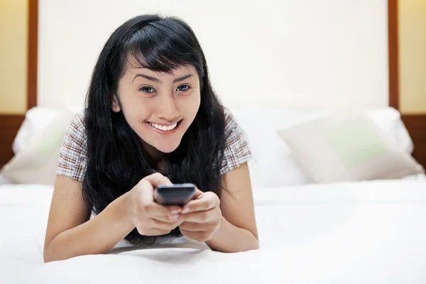 Asian woman with a remote control in a hotel room — Stock Photo, Image
