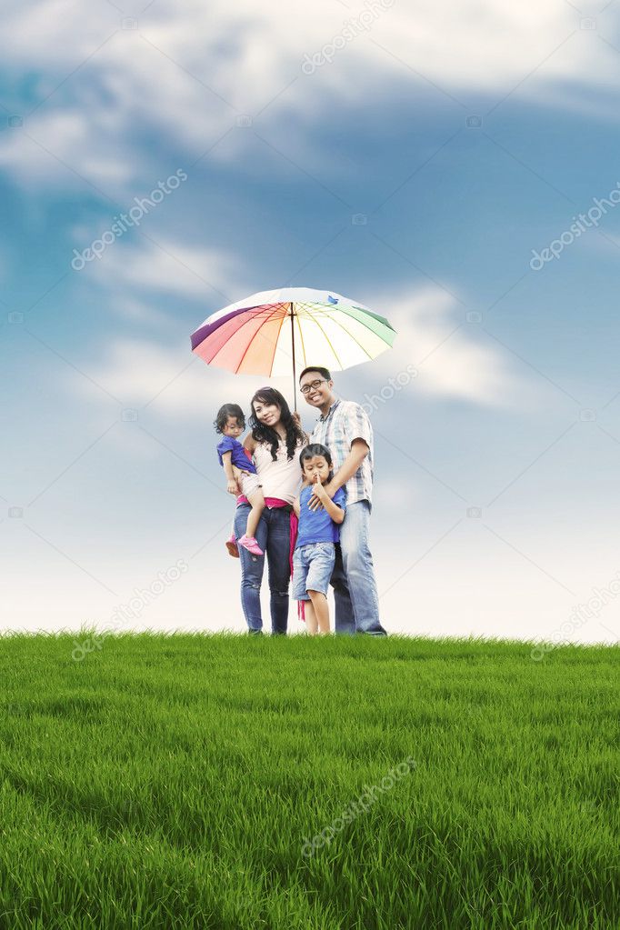 Happy family with colorful umbrella in meadow