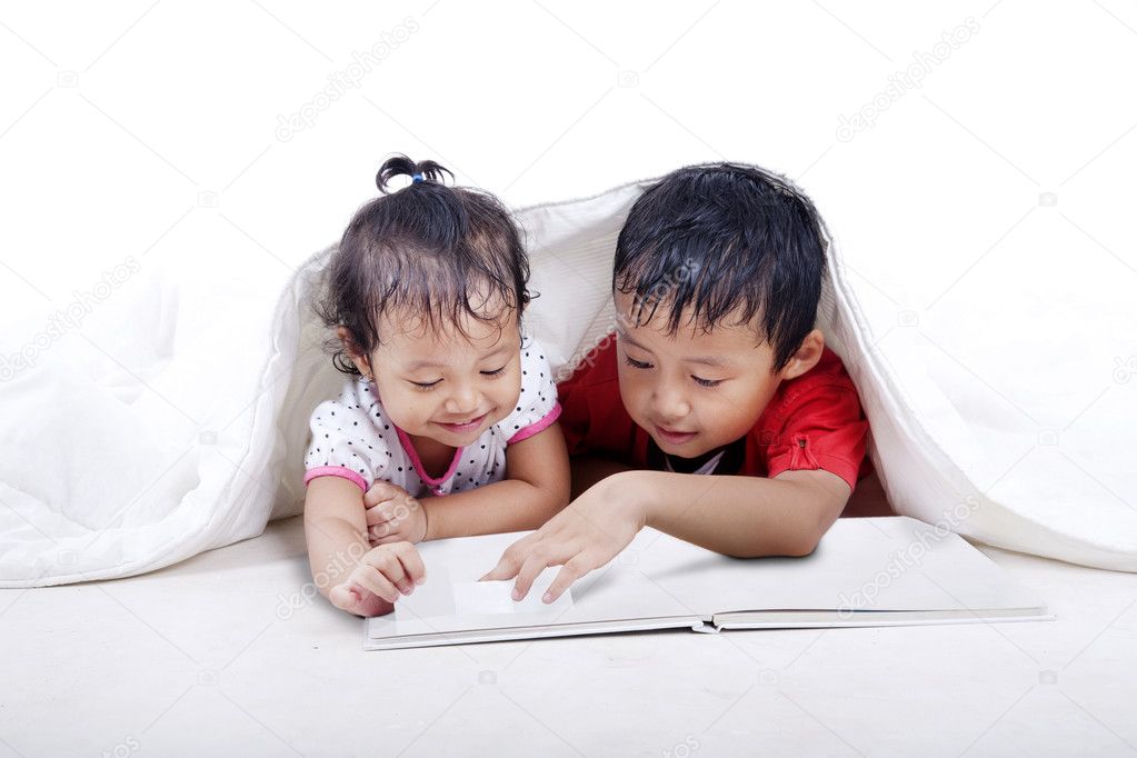 Sibling reading book under the balnket