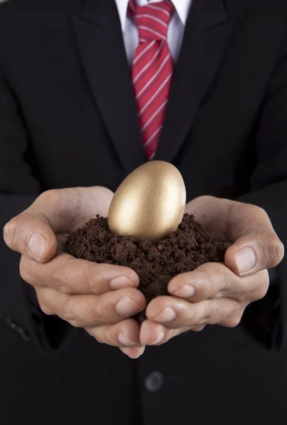 Investment concept businessman with golden egg and soil — Stock Photo, Image