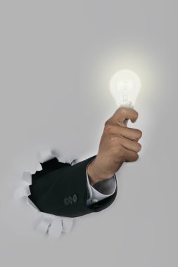 Businessman hand breaking through a paper wall holding light bulb clipart