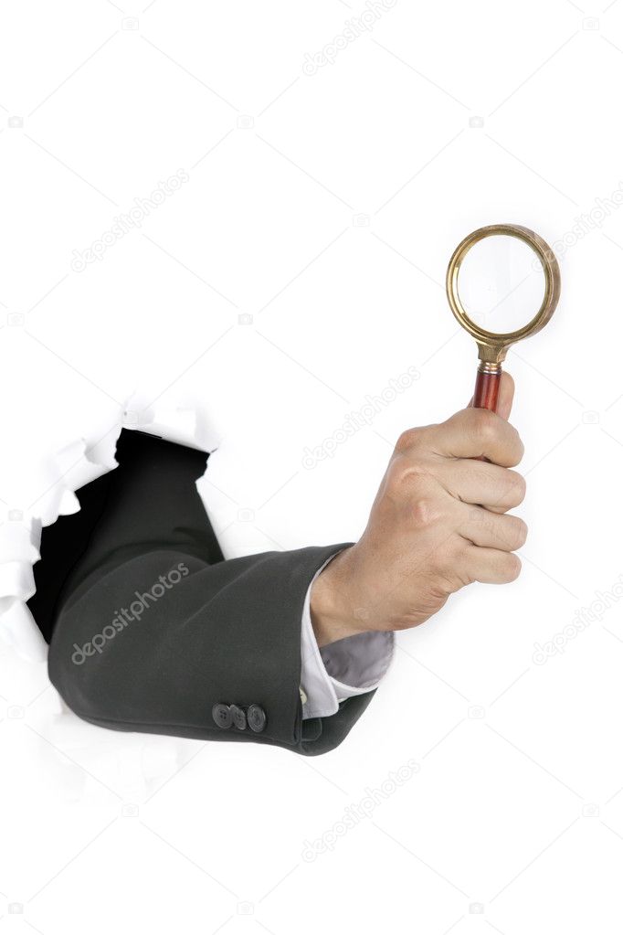 Businessman breaking through a paper wall holding a magnifying glass