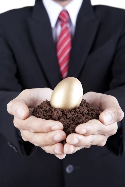 Businessman showing golden egg and soil — Stock Photo, Image