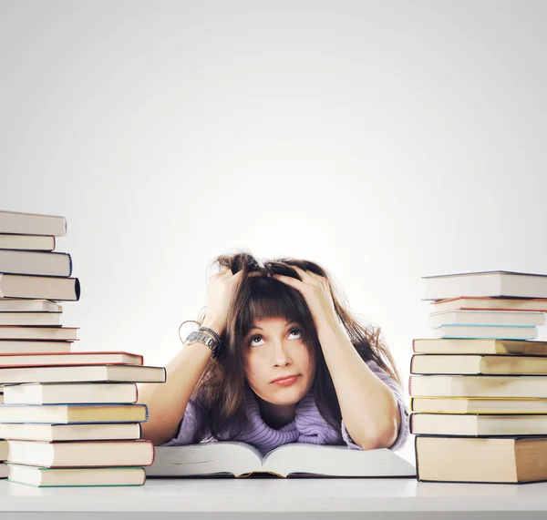 Устав от учебы, молодая женщина сидит на столе с книгами — стоковое фото