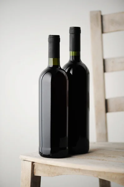 Duas garrafas de vinho tinto em uma cadeira de madeira branca — Fotografia de Stock