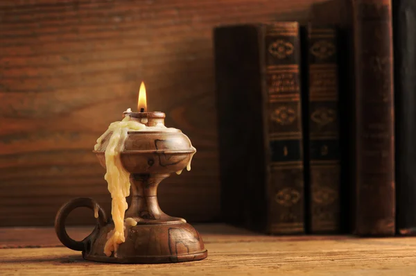 Oude kaars op een houten tafel, oude boeken op de achtergrond — Stockfoto