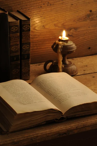 Oud boek op een houten tafel bij kaarslicht — Stockfoto