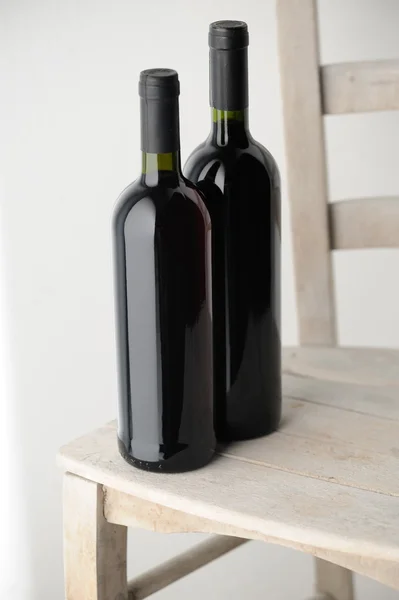 Duas garrafas de vinho tinto em uma cadeira de madeira branca — Fotografia de Stock