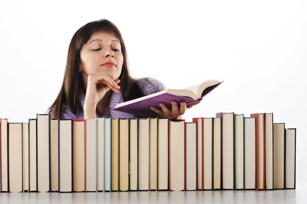 Молодая женщина читает книгу за большой грудой книг — стоковое фото