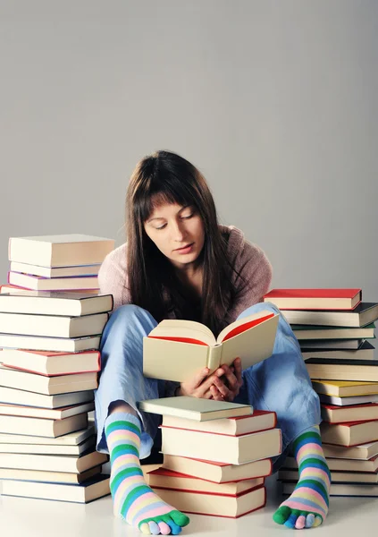Söt flicka studerar med en stor trave böcker — Stockfoto