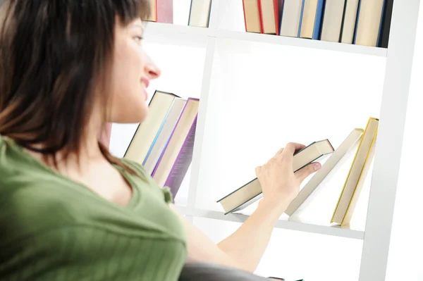 Ung kvinna söker en bok i bokhyllan, liknande Foto — Stockfoto