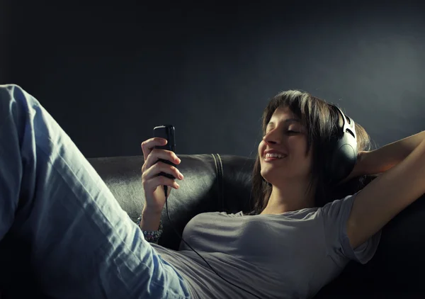 Relajada sonriente mujer acostada en el sofá mientras escucha música en hea —  Fotos de Stock