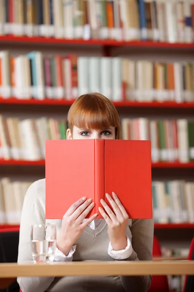 Dívka schovává za knihu o knihovně — Stock fotografie