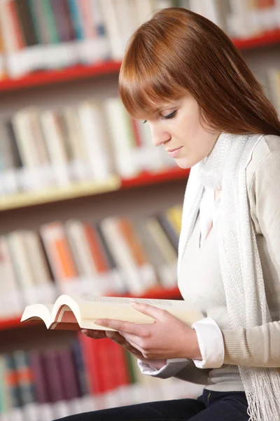 Νεαρός φοιτητής ανάγνωση σε μια βιβλιοθήκη — Φωτογραφία Αρχείου