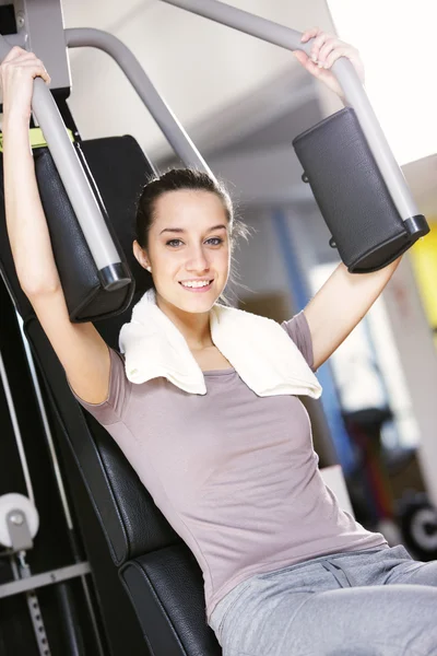 Mujer joven hace ejercicio en la máquina de entrenamiento con pesas — Foto de Stock