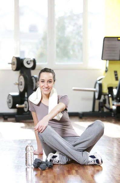 Jonge vrouw zittend op de vloer van de sportschool na workout — Stockfoto