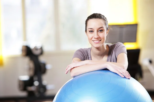 Привлекательная молодая женщина, опирающаяся на мячик для упражнений в спортзале — стоковое фото